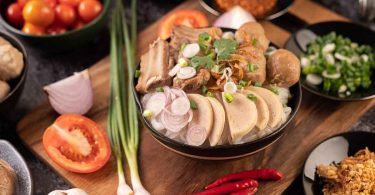 A picture of a person holding chopsticks and a bowl of pho with the text overlay of "Beginner's Guide to Cooking Vietnamese Food at Home: Learn the basics of making delicious and healthy Vietnamese dishes in the comfort of your own kitchen