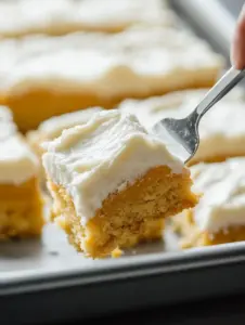 A close-up of a moist pumpkin bar with thick cream cheese frosting being lifted from a baking tray, showcasing its soft texture and creamy topping.